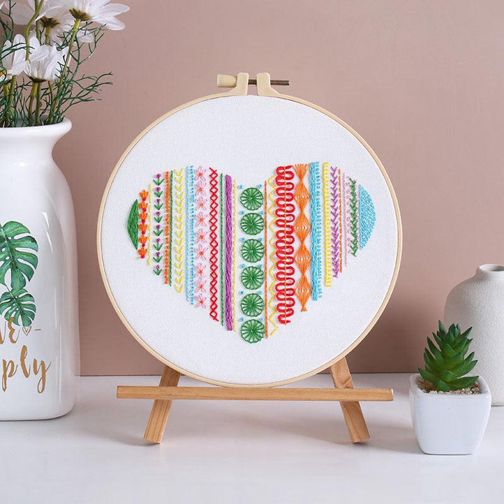 Heart-shaped embroidery displayed on a stand with colorful threads in a hoop, ideal for beginners.