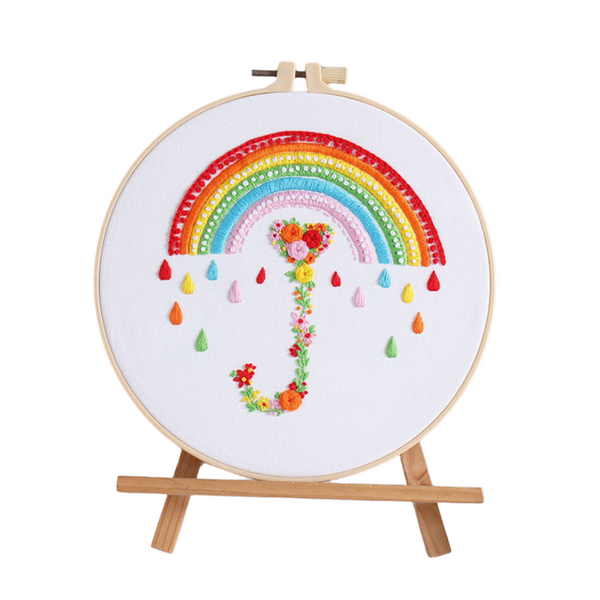 Heart-shaped embroidery kit featuring a colorful rainbow and floral umbrella design on an easel, perfect for beginners.